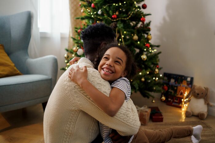 Happy child hugging an adult in front of a Christmas tree, showcasing a family's version of normal for kids.