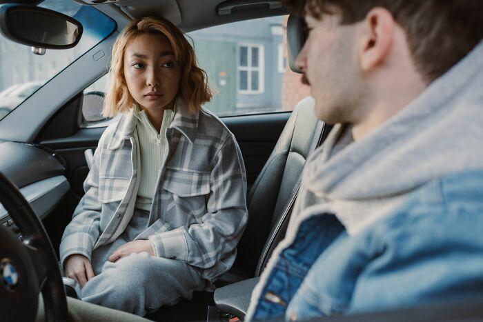 A woman in a car looking suspiciously at a man, noticing cheating red flags.