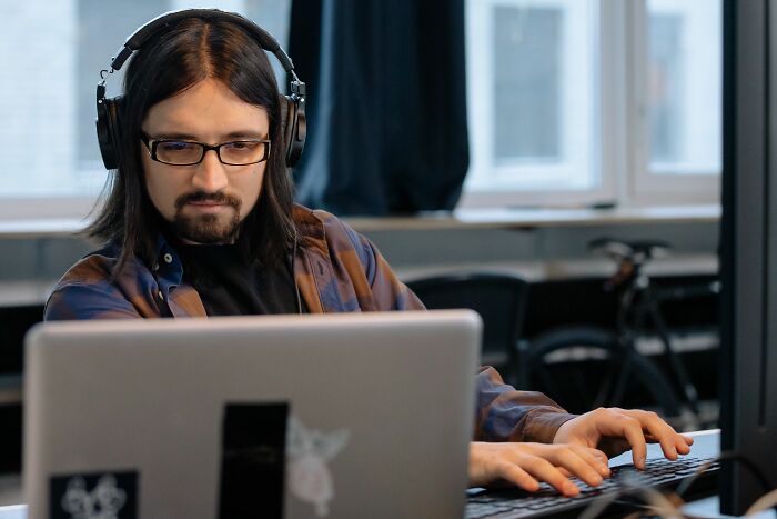 A man with long hair and headphones working on a laptop, a common office story scene.