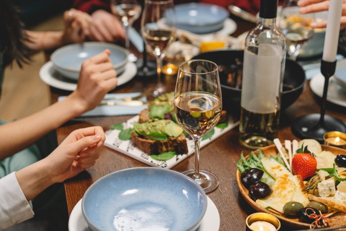 A woman refuses to eat at MIL's home. Focus on a dining table with glasses of white wine and food.