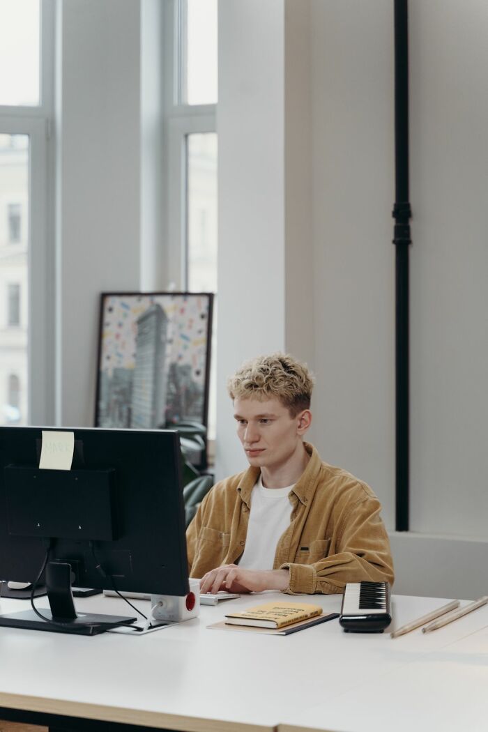 A young man with curly blonde hair working at a computer, focused, highlighting secrets people weren't supposed to know.