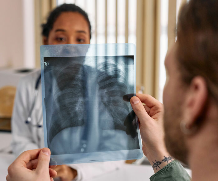 Doctor reviews an X-ray with a patient, highlighting a potential warning sign of pneumonia. Doctor reviews an X-ray with a patient, highlighting a potential warning sign of pneumonia.