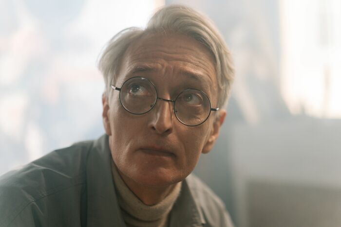 A man with glasses looks up thoughtfully, considering his baby talk. He was once thought perfect.