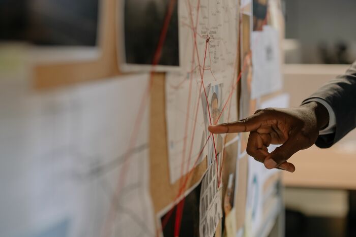 A hand pointing at a hidden pop culture connection board with photos and red strings tying them together. A hand pointing at a hidden pop culture connection board with photos and red strings tying them together.