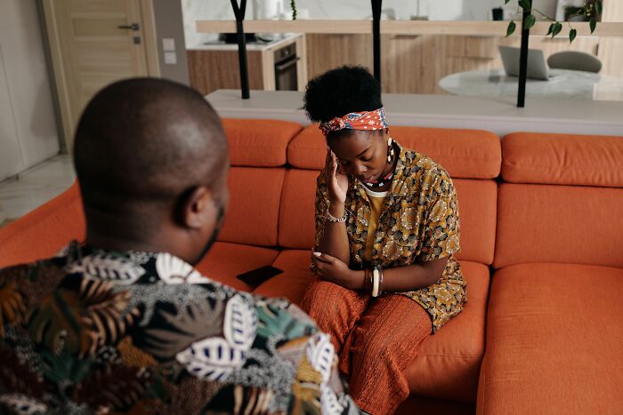 Concerned couple getting married, having a difficult conversation on an orange couch.