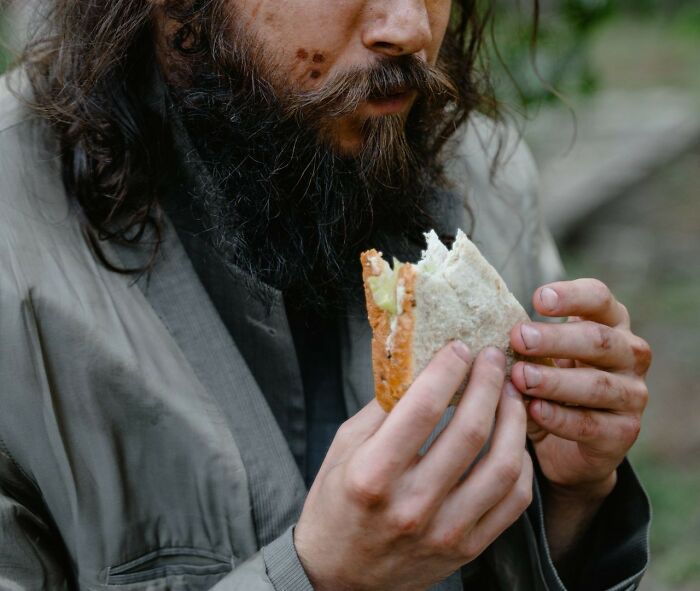 A man with a long beard eating a sandwich, depicting a moment from public horror stories.