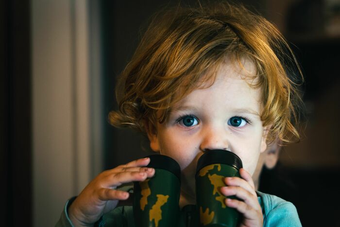 A young child with red hair looks directly at the camera while holding binoculars, depicting parents terrified.