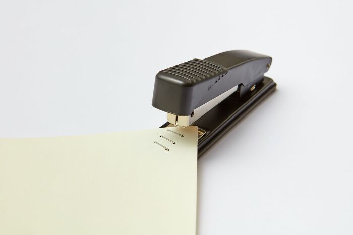 A black stapler stapling a piece of paper, representing the daily HR problems that HR deals with.