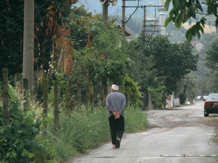 An older man walking away on a rural road with green foliage and power lines. This image represents unusual ways people have lost their lives.