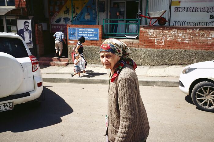 An elderly woman in a patterned headscarf looks at the camera on a street, capturing a moment from public horror stories.