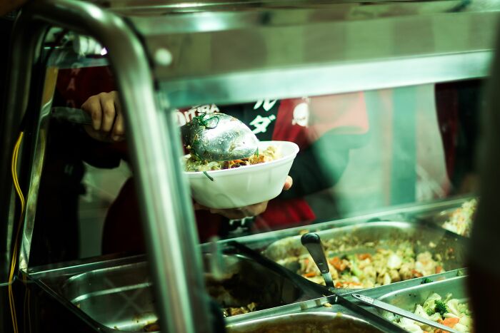 Person serving food from a buffet line, suggesting issues with health inspections and making one happy to be a vegetarian.