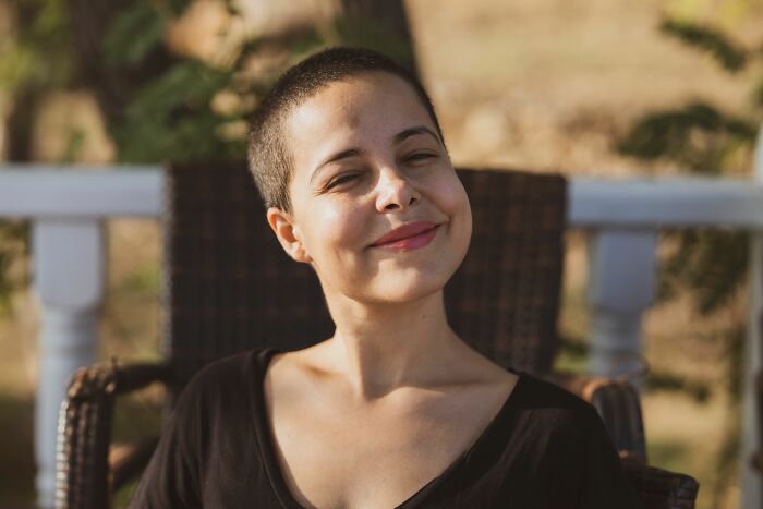 A young woman with a shaved head smiles, reflecting on unexpected twists and turns that changed her life.