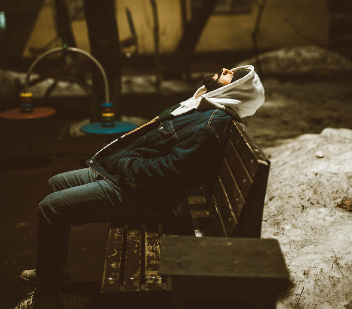 A lonely man with a beard and hoodie sitting on a park bench at night, looking up. A lonely man with a beard and hoodie sitting on a park bench at night, looking up.