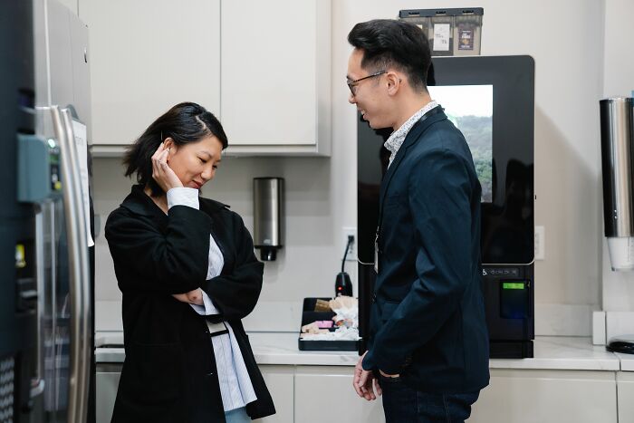 Two socially awkward people having a conversation in a kitchen, potentially sharing cringe moments.