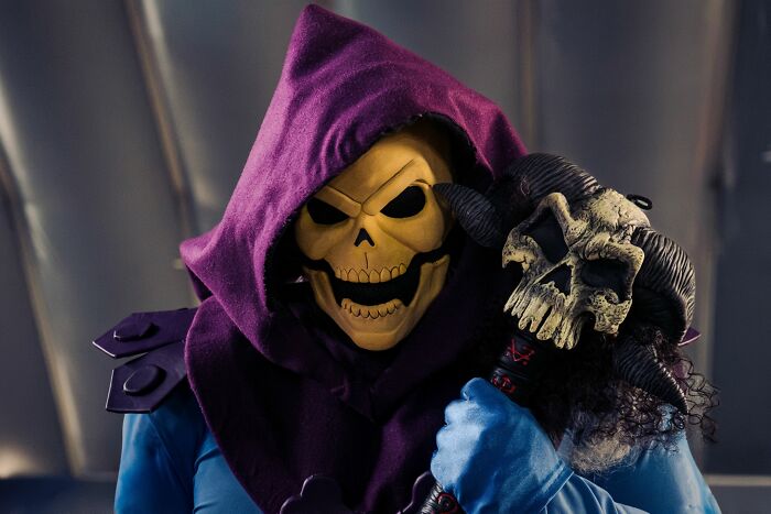 A close-up shot of Skeletor, a villain, in his iconic outfit featuring a purple hood and a skull mask, holding a staff.