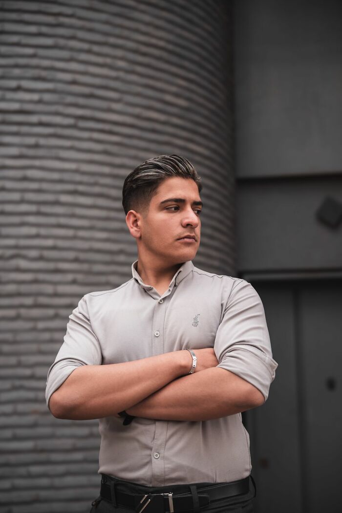 A young man with slicked-back hair, arms crossed, looking away, reflecting on entitled friends.