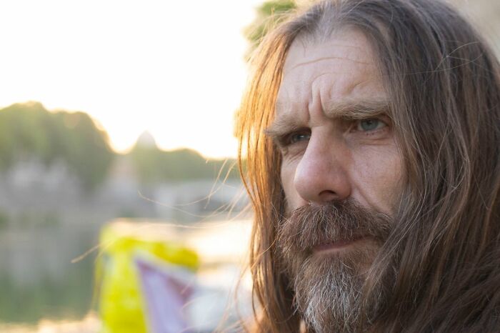 A man with long hair and a beard, looking off into the distance, perhaps contemplating public horror stories.