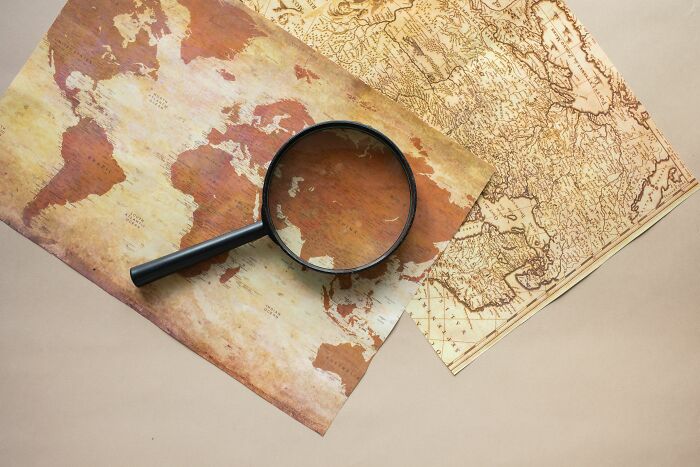 A magnifying glass lies on top of two vintage world geography maps, one displaying the continents, for an article about geography questions. A magnifying glass lies on top of two vintage world geography maps, one displaying the continents, for an article about geography questions.