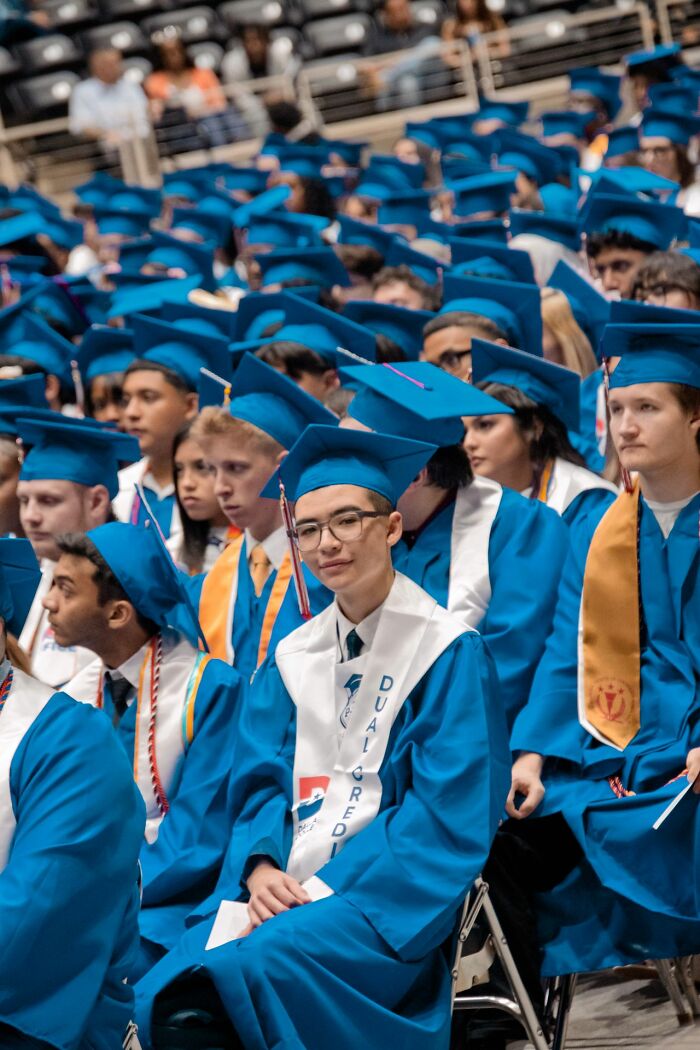 Graduates in blue caps and gowns sitting in an audience, a behind the scenes look at education achievements.
