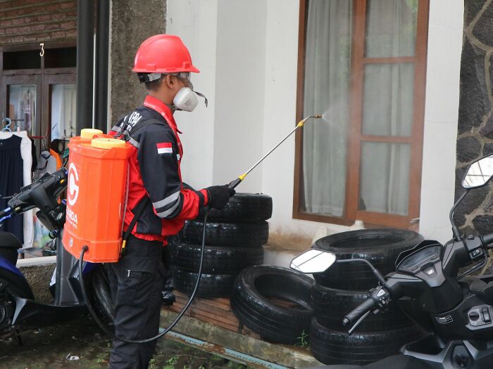 Worker in a red helmet spraying disinfectant near tires and bikes, highlighting industry secrets in sanitation jobs.