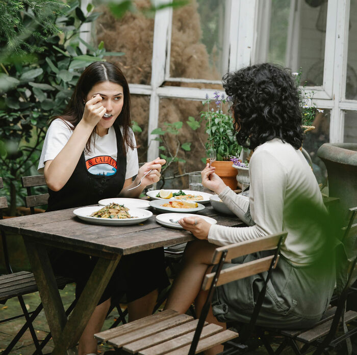 Two women enjoying a meal at an outdoor cafe, discussing the side effects of trendy snack food.