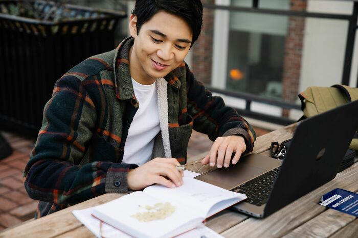 A young man working on a laptop and notebook, perhaps checking for pocket dial incidents.