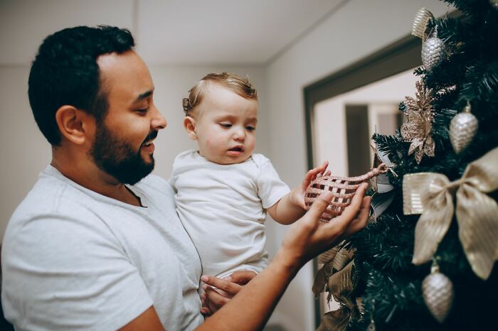 A father and baby decorating a Christmas tree, sharing hidden family secrets.