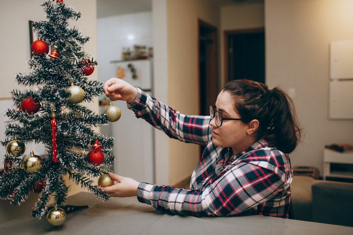 A woman decorating a small Christmas tree, potentially trying to distract from the worst MILs.