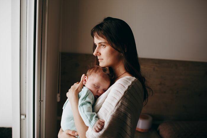 A thoughtful mother holds her sleeping infant, perhaps contemplating stories about MILs who are the worst.