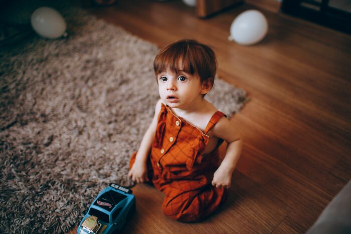 A child with red hair sitting on a wooden floor, looking up with a surprised face, showing moments parents were terrified of their children.
