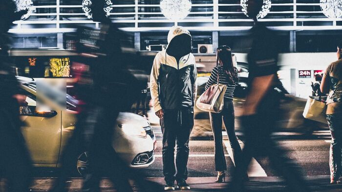 A lone figure in a hoodie standing on a busy city street at night, highlighting disturbing facts about urban isolation.