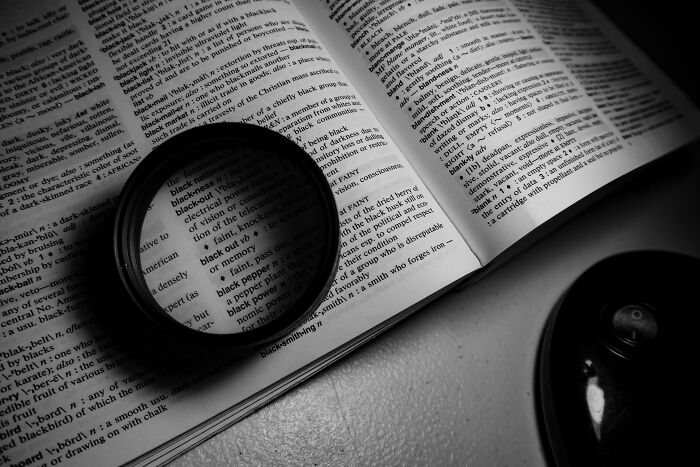 Magnifying glass on an open dictionary showing advanced English words. It's for advanced speakers to learn smart words.