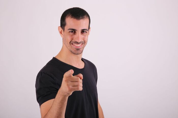 A man smiling and pointing towards the viewer, embodying stereotypically white phrases that crack people up.