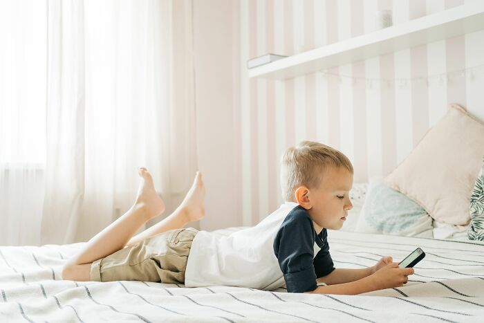 Parenting expert observes a child on a bed using a phone, showing kids understanding and confusion.