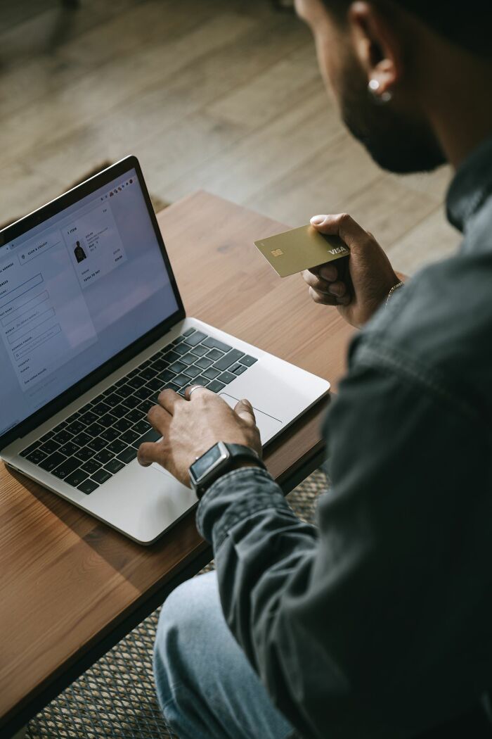 A man holding a gold credit card and typing on a laptop, indicating behind the scenes secrets companies don't want you to know.