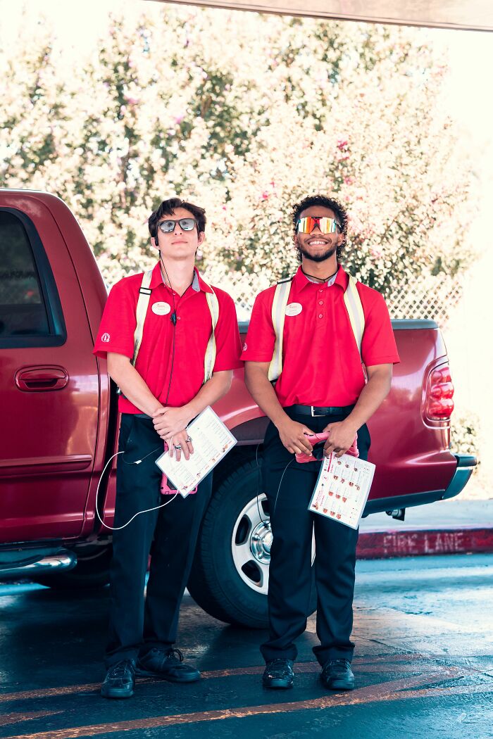Two young men in red shirts and vests stand by a red truck, possibly on their final day at work.