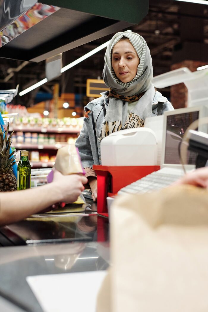 A woman in a hijab at a grocery store checkout, representing everyday transactions that hide behind the scenes secrets companies don't want you to know.