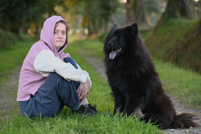 A person in a hoodie sits with a large black dog, representing unexpected twists and turns that changed their lives.