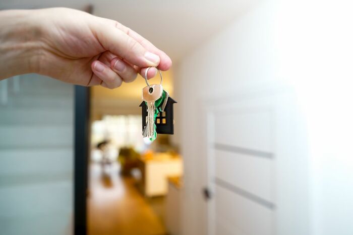 Hand holding house keys with a house-shaped keychain, symbolizing behind the scenes secrets in real estate companies.