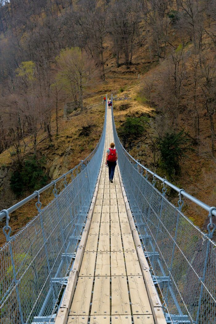 A person with a red backpack walks on a suspension bridge, reflecting a scene related to stereotypically white phrases.