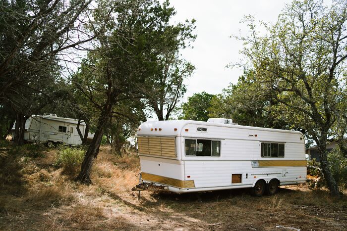 Two old travel trailers parked in a grassy, wooded area, representing a family's version of normal for kids visiting a friend's house.