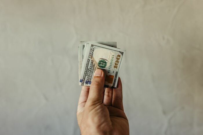 A hand holding a stack of US 100 dollar bills, symbolizing American habits.