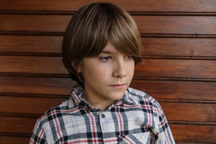 A young boy with brown hair and a plaid shirt looks thoughtfully, portraying a child parents were terrified of.