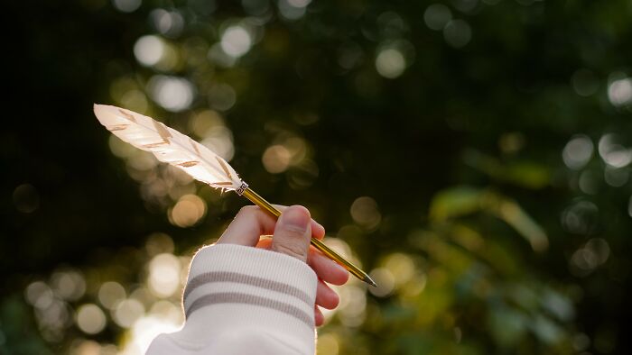 A hand holding a quill pen against a bokeh background, representing the concluding words and endings of films, books, and songs. A hand holding a quill pen against a bokeh background, representing the concluding words and endings of films, books, and songs.