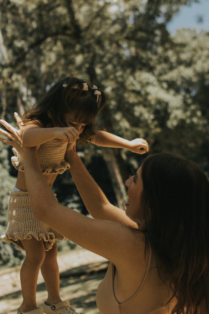 A mother lifting her young daughter in the air outdoors, showcasing moments that changed people's lives.