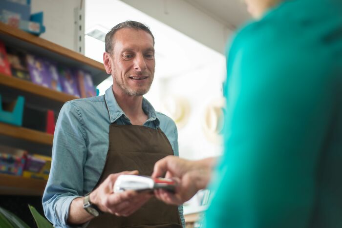 A smiling man in an apron is receiving payment, a scene from a final day at work.