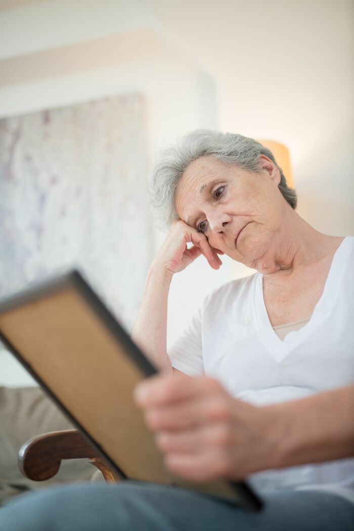 A senior woman looks sadly at a framed photo, reflecting on unexpected twists and turns that changed people's lives.