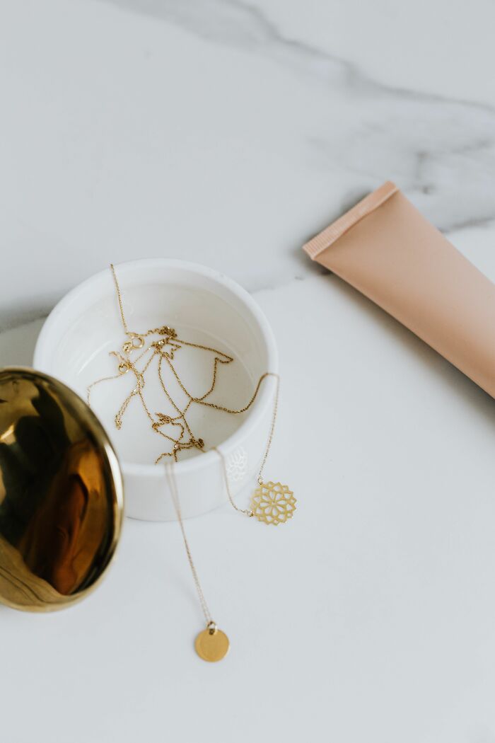 Gold necklaces and a cosmetic tube on a marble counter, reflecting industry secrets about beauty jobs.