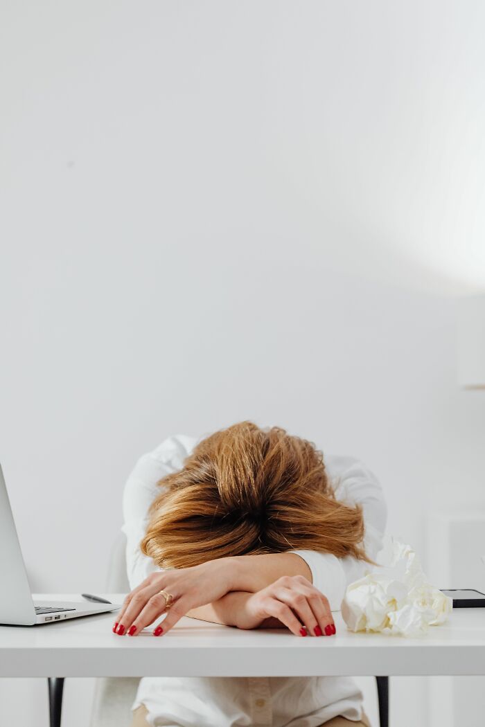 A woman with her head down on her arms on a desk, next to a laptop and crumpled paper, symbolizing the final day at work.