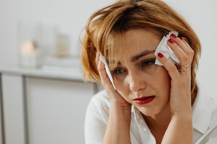 A woman distraught, holding tissues to her face, revealing small cheating red flags.